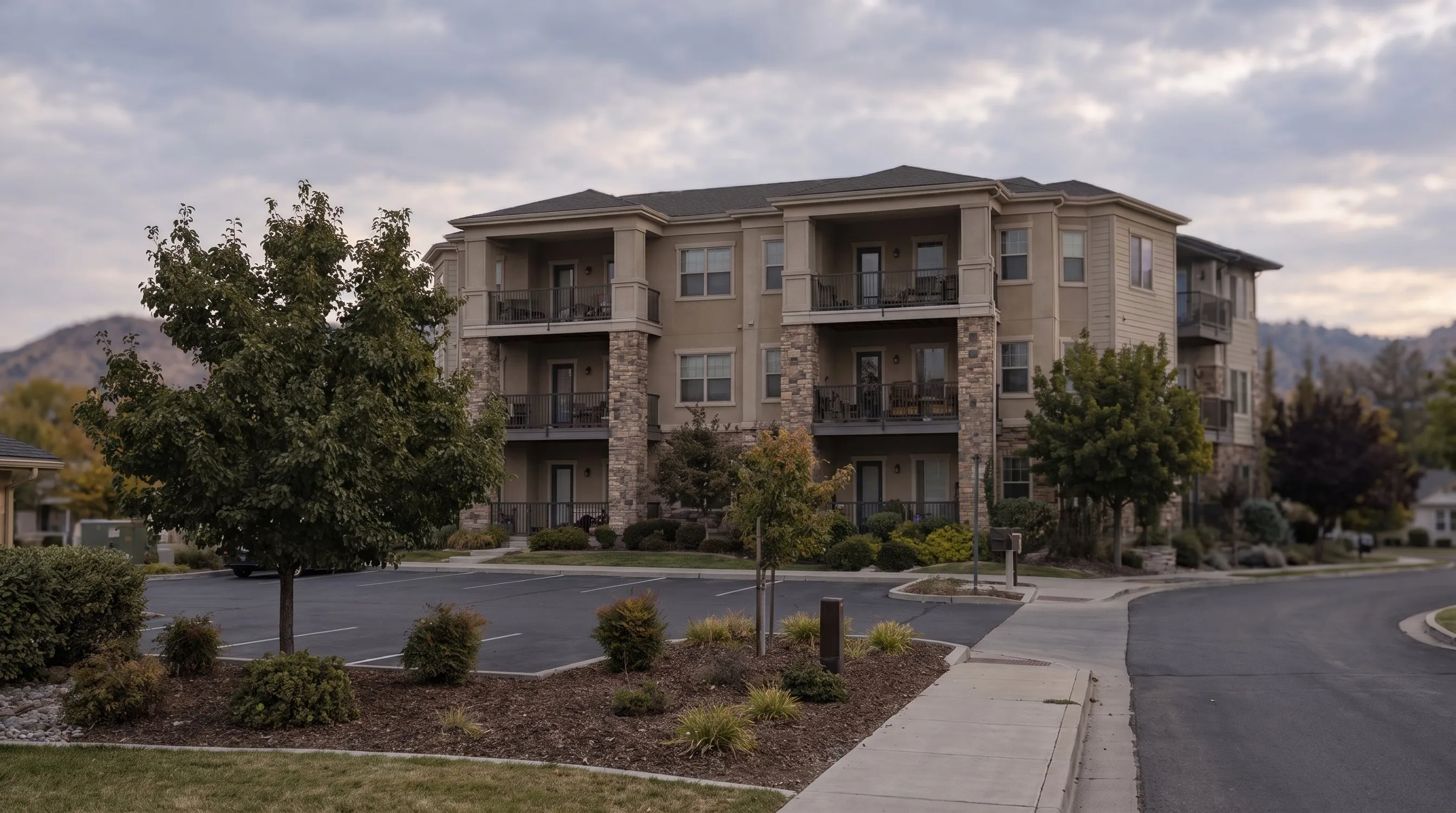 A three-story condominium building with balconies and a parking lot in front.