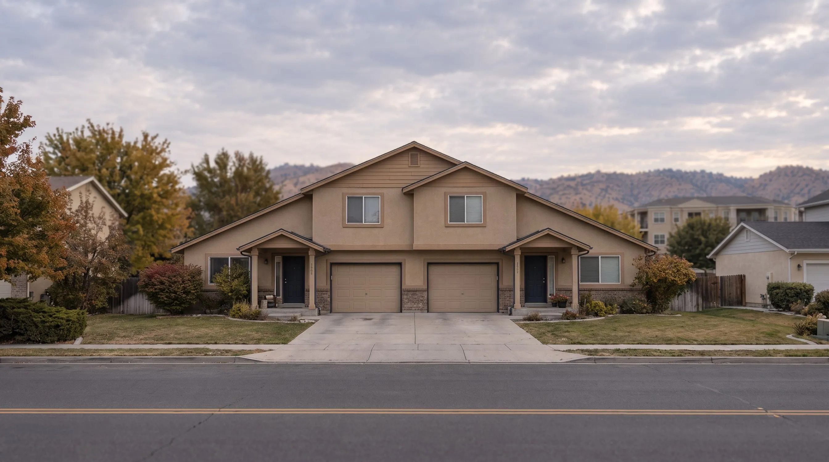A two-story side-by-side duplex with two front doors and two garage doors.