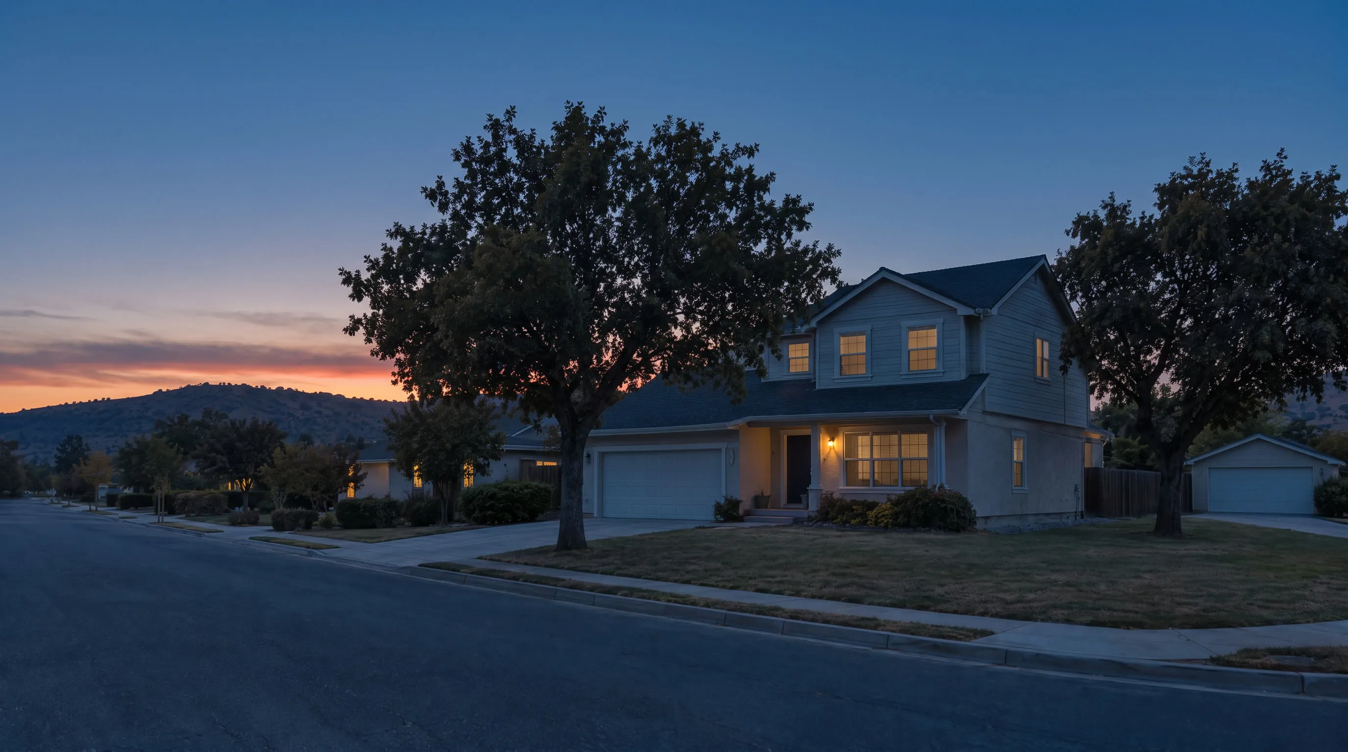 The house at dusk, the porch lantern and windows lit, the ridge dark under a deep blue sky.