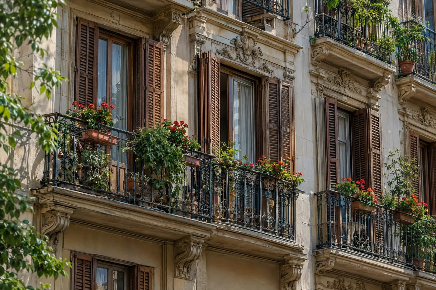 An ornate apartment facade with wrought iron balconies, tall wooden shutters and potted geraniums.