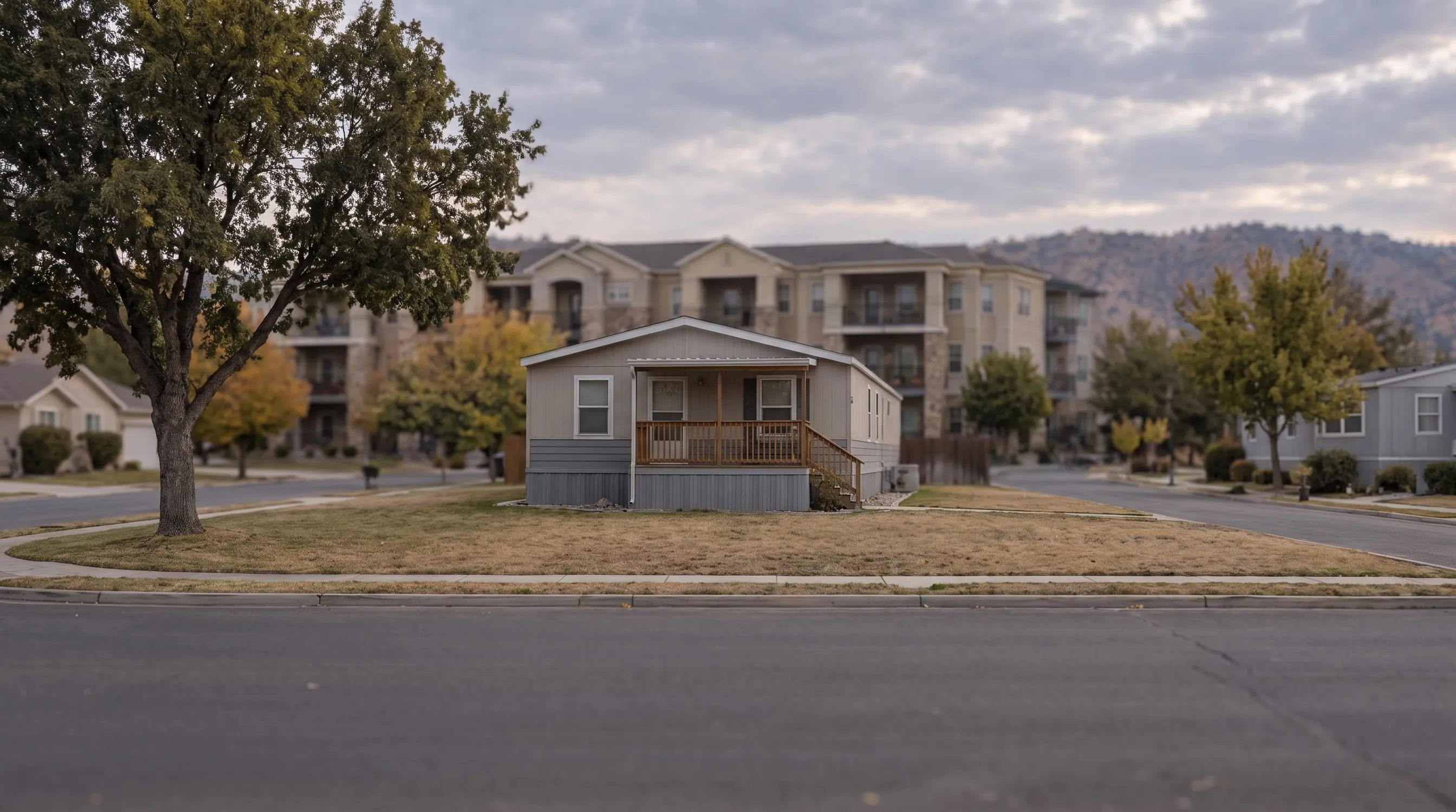 A single-wide manufactured home with a covered wooden porch on its own lot.