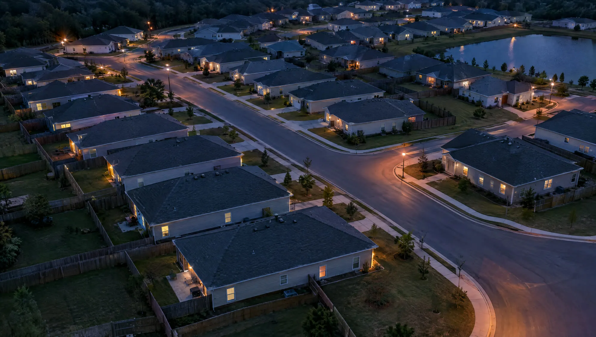 Aerial view at dusk of a subdivision of near-identical single-story homes on curving streets.